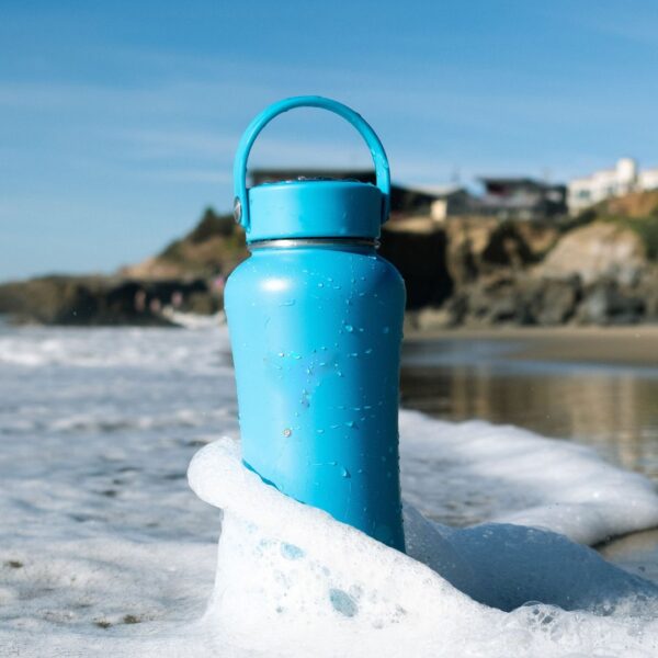 An insulated tumbler on a beach getting splashed by a wave